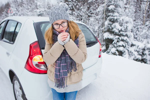 Young woman stays on a snow-covered winter road next to the car and warms her hands. — Stock Photo, Image