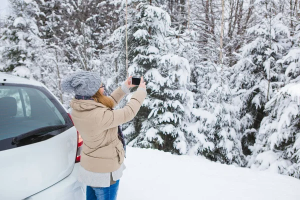 Jonge vrouw neemt foto van besneeuwde winter forest. — Stockfoto