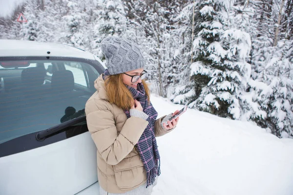 Jovem mulher de pé ao lado do carro em um fundo de floresta de inverno coberta de neve . — Fotografia de Stock