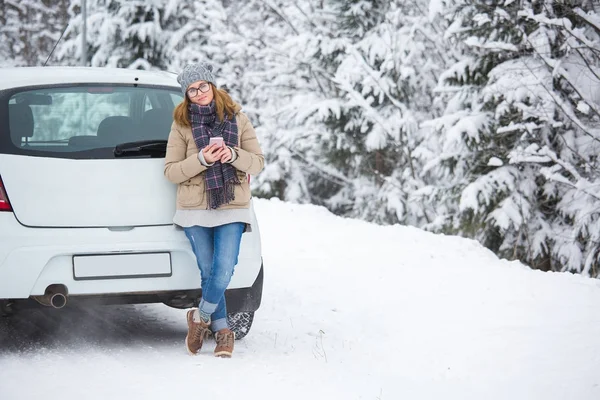 Giovane donna in piedi accanto alla macchina su uno sfondo di foresta invernale innevata . — Foto Stock