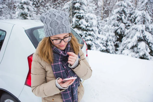 Jovem mulher de pé ao lado do carro em um fundo de floresta de inverno coberta de neve . — Fotografia de Stock