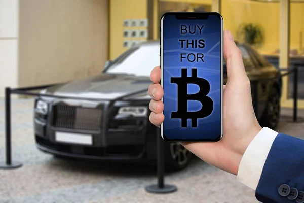Kézzel, egy ember, és a telefon, a háttérben egy luxus autó. A képernyőn van a felirat "vásárolni ezt a bitcoin" — Stock Fotó