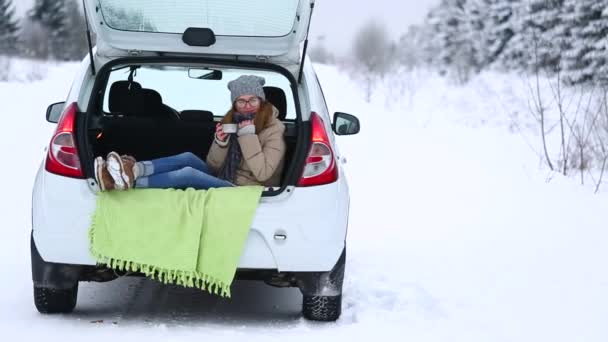 女性旅行者は車のトランクに座って 熱いお茶を飲みます 冬の森 雪に覆われた木 — ストック動画