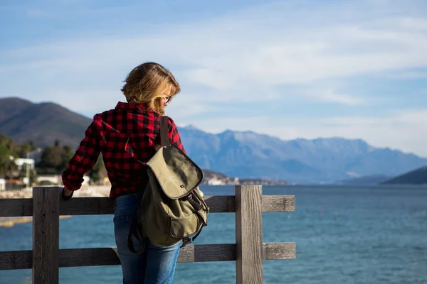 Mulher em uma camisa com uma mochila está de pé em um cais de madeira — Fotografia de Stock