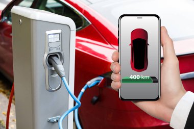 Hand with phone on a background of electric car charging point.  clipart
