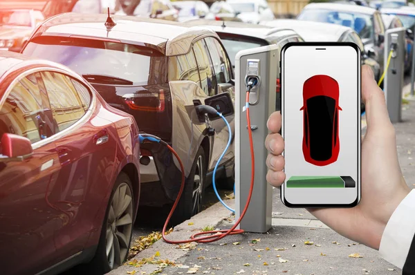 Hand mit Telefon auf dem Hintergrund einer Ladestation für Elektroautos. — Stockfoto
