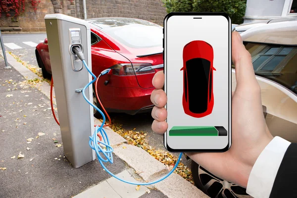 Hand with phone on a background of electric car charging point. — Stock Photo, Image