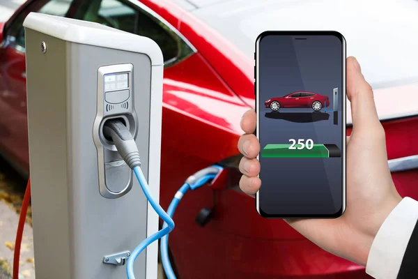 Hand with phone on a background of electric car charging point. — Stock Photo, Image