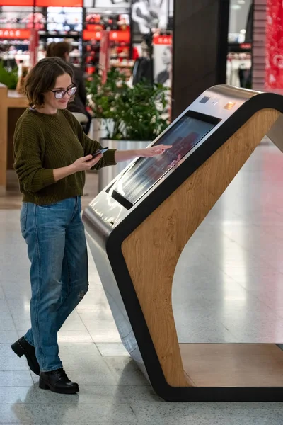 Woman with phone uses self-service kiosk in the shopping mall