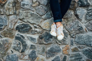 kadının bacakları ile taş duvarda oturan spor ayakkabı.