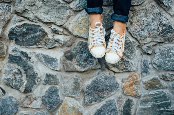 Kvinnans ben med sneakers sittande i stenmur. — Stockfoto