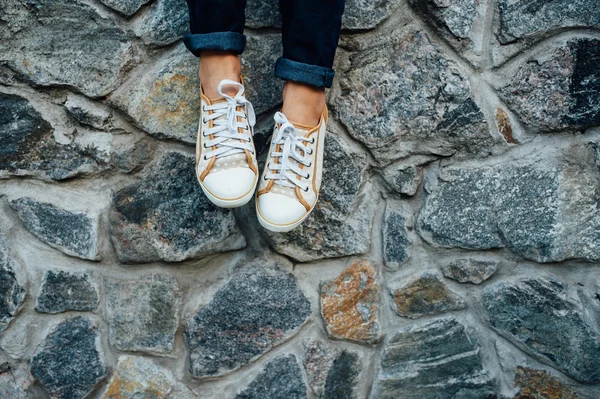 Kvinnans ben med sneakers sittande i stenmur. — Stockfoto