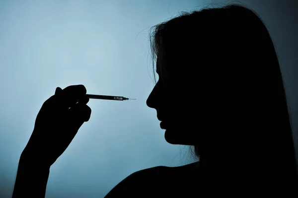 Syringe and girl silhouette on a blue background — Stock Photo, Image