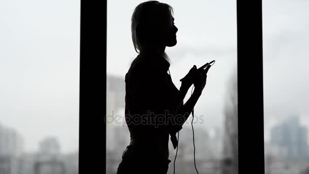 Sexy, happy woman listening to music and dancing by window at home. — Stock Video