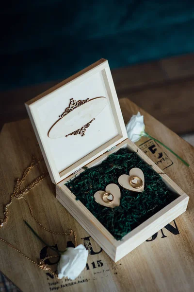 两个金光闪闪的结婚戒指挂在绿叶装饰木盒上 — 图库照片
