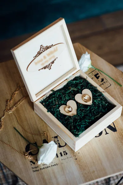 两个金光闪闪的结婚戒指挂在绿叶装饰木盒上 — 图库照片