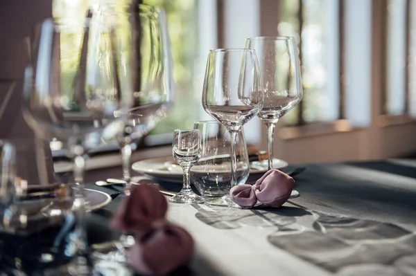 Glasses, flowers, fork, knife served for dinner in restaurant with cozy interior, — Stock Photo, Image