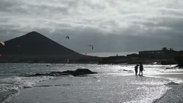 Veel kleurrijke vliegers op het strand en kitesurfers paardrijden golven tijdens winderige dag — Stockvideo