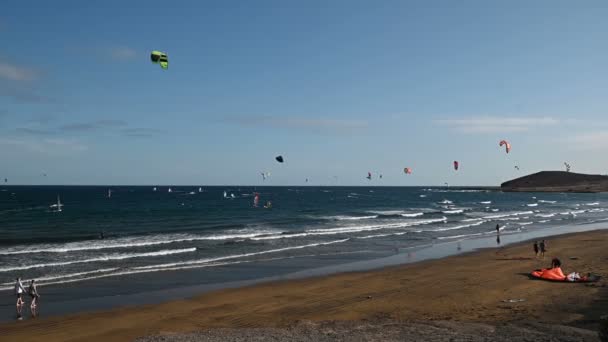 Mnoho barevných draků na pláži a drak surfaři na koni vlny během větrného dne — Stock video