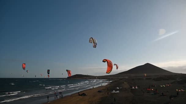 Många färgglada drakar på stranden och kitesurfare rider vågor under blåsig dag — Stockvideo