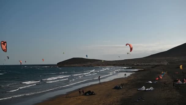 Muitos papagaios coloridos na praia e kitesurfistas montando ondas durante o dia ventoso — Vídeo de Stock