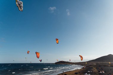 Birçok renkli uçurtma sahilde ve uçurtma sörfçüleri rüzgarlı bir günde dalgalara binerler.