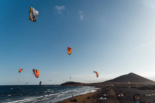 Many colorful kites on beach and kite surfers riding waves during windy day — Stock Photo, Image