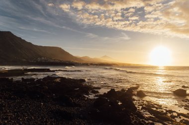 Okyanus üzerinde uçan dalgalar güzel günbatımına ve ufuktaki dağlara bakıyor..