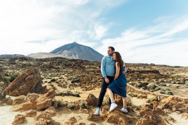 Bir volkanın arka planında kayalık bir tarlada poz veren güzel genç aşıklar.