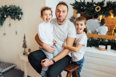 happy father hugs his sons. Photo taken in an apartment with a Christmas tree