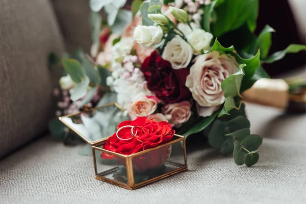 На скляному столі в кімнаті коробка з обручками, поруч з нею букет квітів — стокове фото