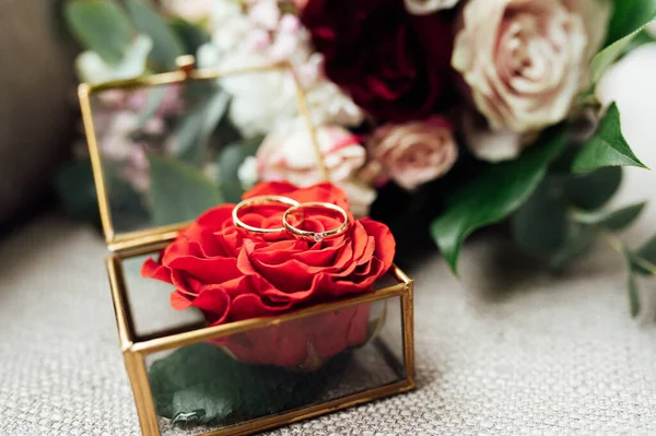 На скляному столі в кімнаті коробка з обручками, поруч з нею букет квітів — стокове фото