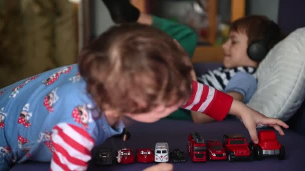 Um adolescente joga ao telefone com fones de ouvido, e o irmão mais novo joga um brinquedo um carro — Vídeo de Stock