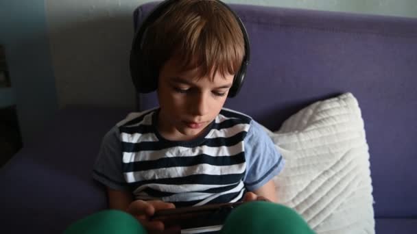 Portrét uvolněného dospívajícího chlapce sedícího na pohovce s chytrým telefonem. — Stock video