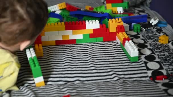 Ευτυχισμένο παιδί παίζει στα χρωματιστά μπλοκ σε ένα ριγέ καναπέ — Αρχείο Βίντεο