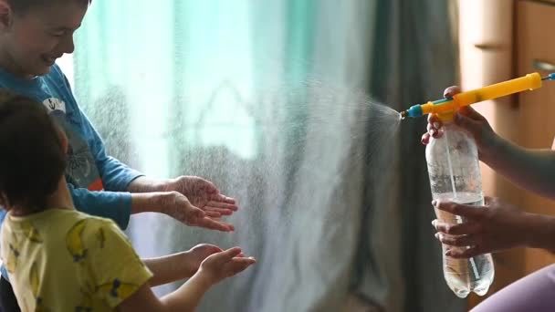 Mãe pulveriza um spray anti-séptico em suas mãos para seus filhos para desinfectar — Vídeo de Stock
