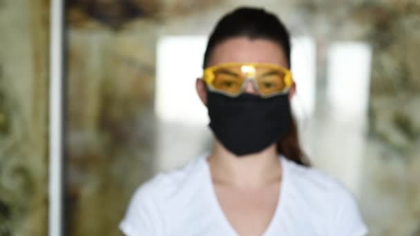 Una niña con una máscara protectora, gafas y guantes rocía un antiséptico para prevenir la infección . — Vídeo de stock