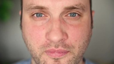 Mavi gözlü, gözlüklü yakışıklı bir adam kameraya bakıyor. Gözlük takar ve gözlerini ovar.