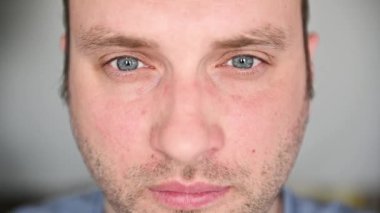 Mavi gözlü, gözlüklü yakışıklı bir adam kameraya bakıyor. Gözlük takar ve gözlerini ovar.