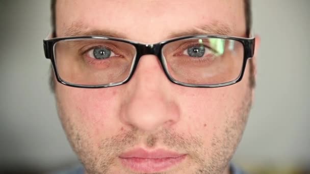 A handsome guy in glasses with blue eyes looks at the camera. Uses glasses and rubs his eyes — Stock Video