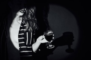 Yeşil arka plandaki kız bir bardak kırmızı içecekle şarap dumanı yana bakıyor.