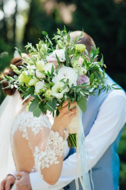 Neşeli yeni evliler düğünlerinde sarılıyorlar ve yüzlerini bir düğün buketi ile kaplıyorlar.