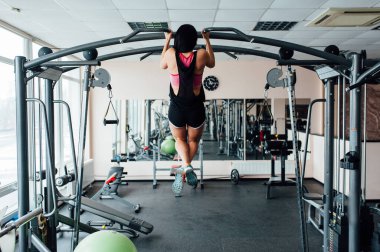 sexy young fitness girl pulls up in the gym. Brunette fitness woman in black sport wear