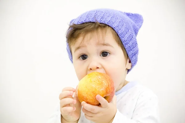 Lindo poco caucásico chico 11 meses de edad se sienta y come rojo manzana en blanco fondo — Foto de Stock