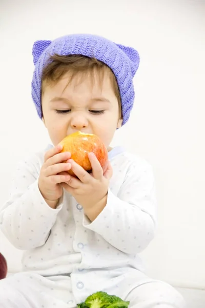 Niño feliz bebé sentado en pañal y comiendo ojos azules manzana verde mirando a la esquina aislado sobre un fondo blanco — Foto de Stock