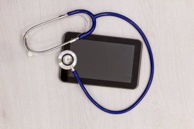 tıbbi teknoloji tablet ve ön planda stetoskop kavramı. Office nesneleri ahşap masa üzerinde online tıbbi konsültasyon konseptiyle tablet ekranında. Yukarıdan görüntülemek