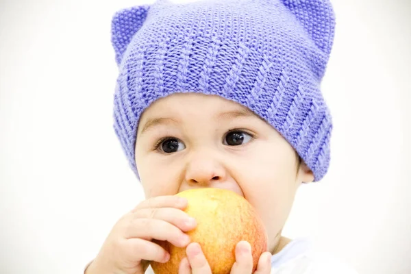 Niño sentado en la mesa con frutas y verduras y comiendo una manzana aislada sobre fondo blanco — Foto de Stock