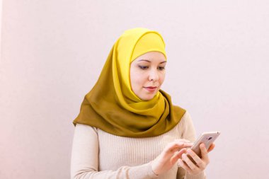 Evdeki kanepede otururken akıllı telefonuyla mesaj atan gülümseyen Müslüman bir kadının portresi.