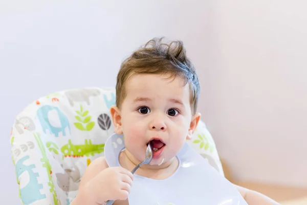 Mosolygó gyerek étkezés konyha. 1 év régi baba enni a saját leves. az első szilárd ételek, hogyan lehet megtanítani a gyermek enni, kanállal. aranyos baba eszik kanállal ebédre — Stock Fotó