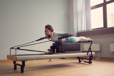 Leotard egzersiz pilates eğitimi. Atletik pilates yenilikçi egzersizleri. Pilates makinesi ekipmanı. Genç Asyalı kadın bir stüdyoda esneme sporu yapıyor.